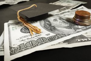 Graduation cap on top of a one-hundred-dollar bill and by smaller bills and change reflecting financial aid received by completing FAFSA