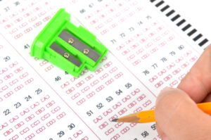 Scantron with pencil sharpener on it and a hand holding a pencil.